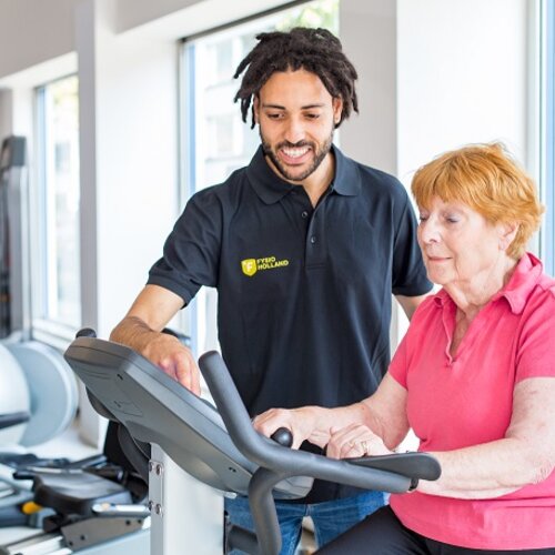 Foto van fysiotherapeut naast client op een fitnessapparaat