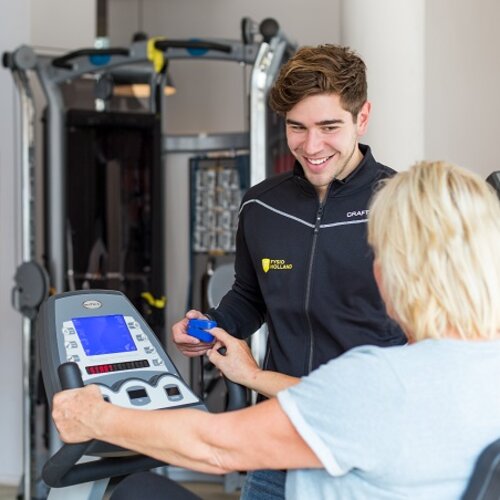 Foto van fysiotherapeut naast een client op een fitnessapparaat