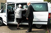 Foto van een vrouw die in een taxibus stapt met hulp van de chauffeur
