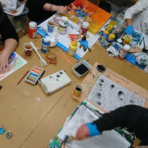 Foto van een aantal mensen aan tafel die aan het schilderen zijn.