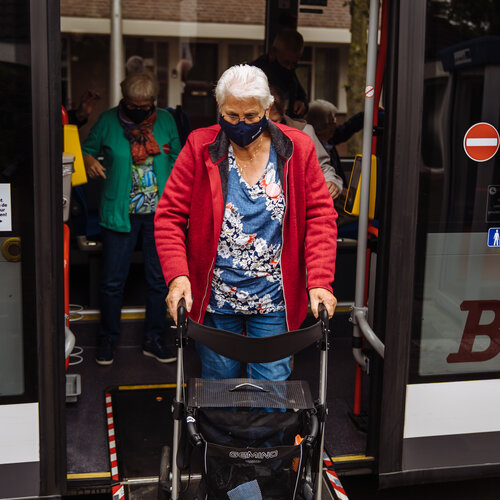 Foto van vrouw die met rollator via een loopplank de bus verlaat