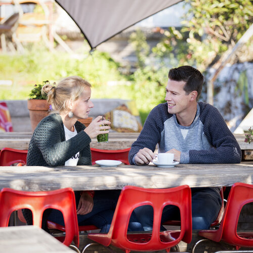 Foto van jonge vrouw en man in gesprek aan een tuintafel