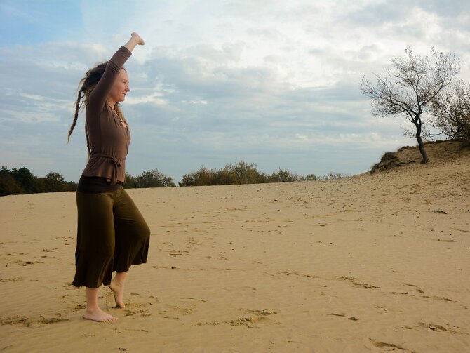 Foto van een vrouw in de duinen die QI Chong beoefent